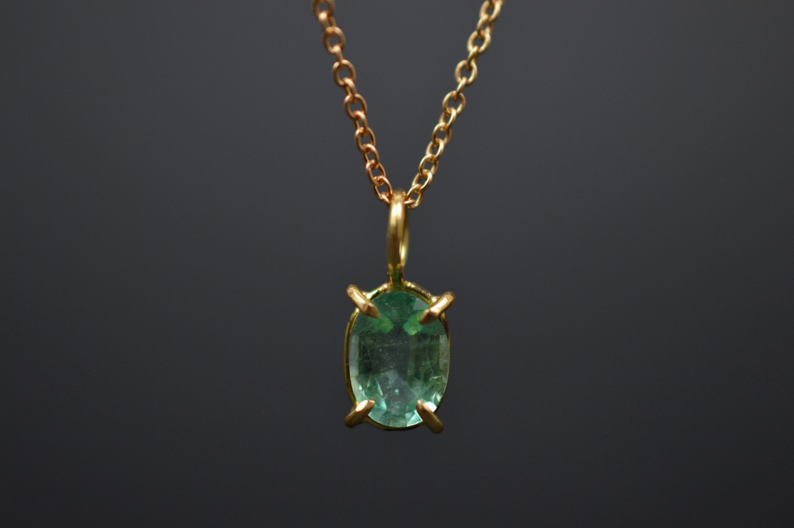 A photo of necklace featuring an emerald pendant, set in 18k gold